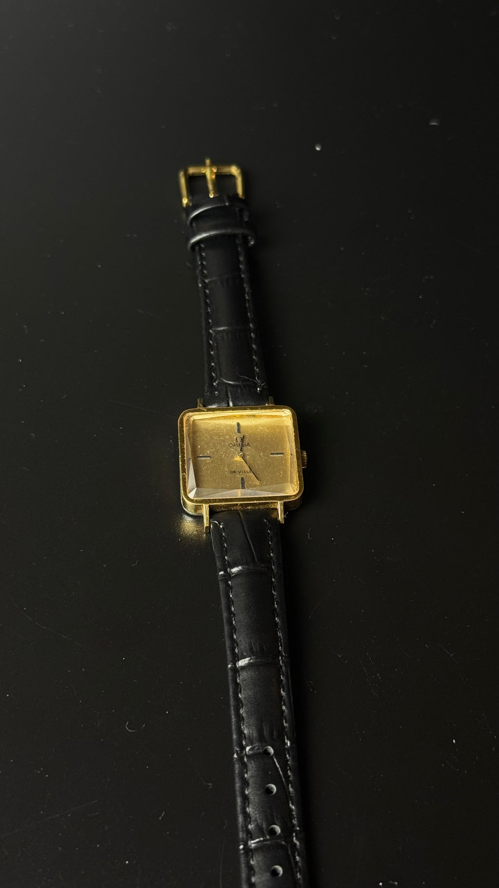 Omega De Ville – kwadratowa koperta, złota tarcza, czarny pasek