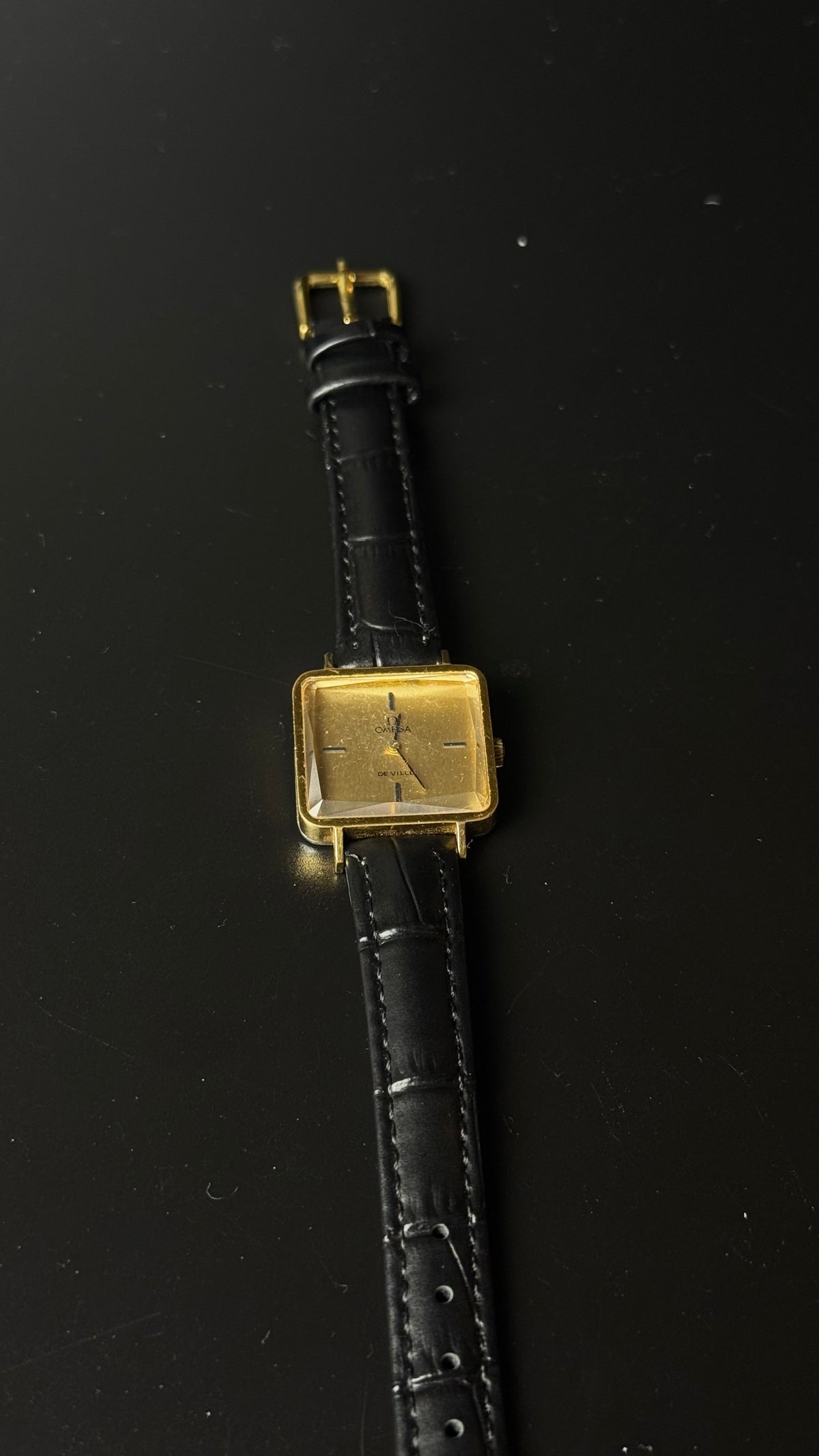 Omega De Ville – kwadratowa koperta, złota tarcza, czarny pasek